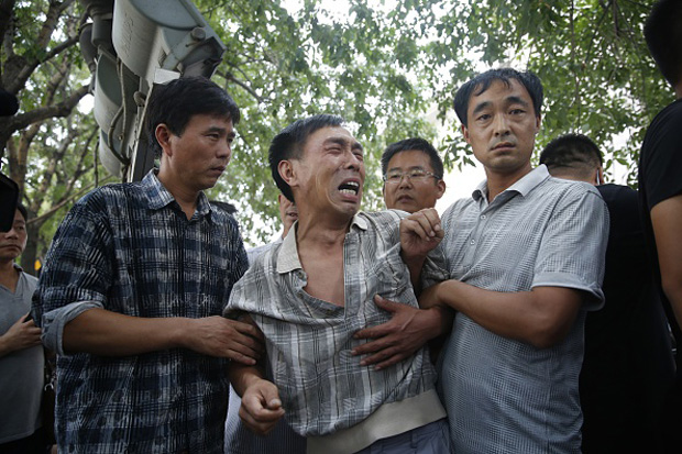 The husband (center) of a woman killed during the explosions at a chemical warehouse is pulled away by staff Aug. 16 as he protests outside a hotel where authorities are holding a press conference in Tianjin.