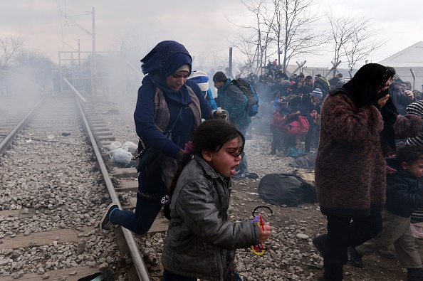 Migrants and refugees run away from tear-gas and stun grenades after Macedonian police fired tear gas at hundreds of Iraqi and Syrian migrants who tried to break through the Greek border fence in Idomeni, on February 29.