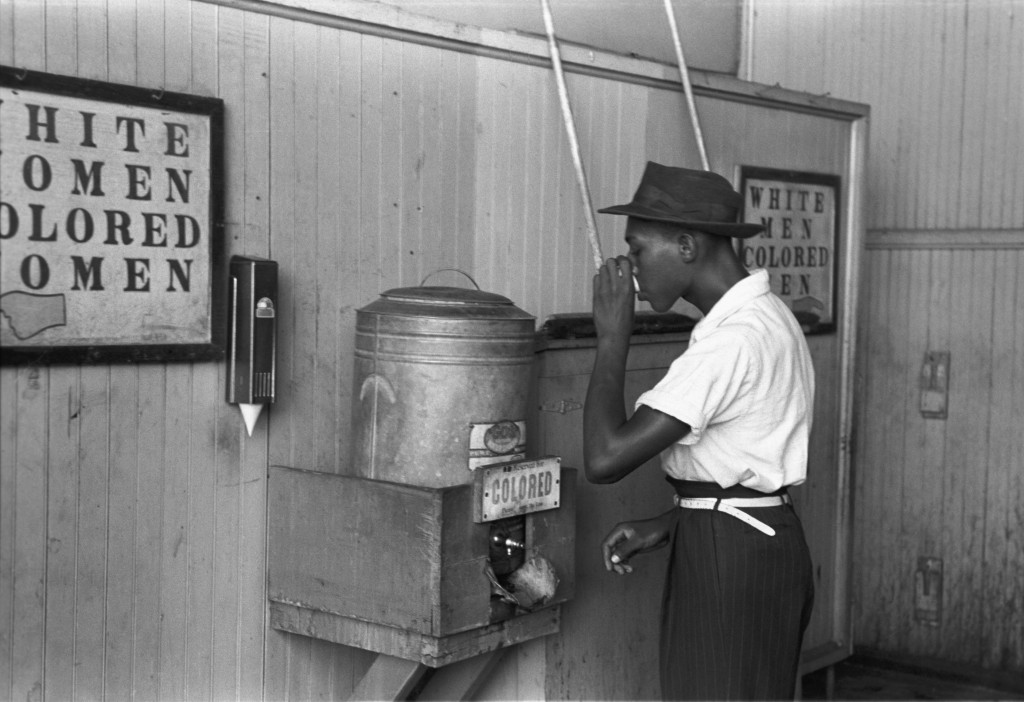 In Oklahoma City in 1939, a black man drinks from a "colored" drinking fountain.