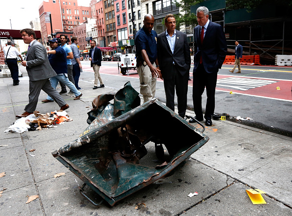 New York Mayor Bill de Blasio (R) and New York Governor Andrew Cuomo (C) stand in front of a mangled dumpster on September 18 while touring the site of an explosion that occurred on Saturday night in the Chelsea neighborhood of New York City. The explosion in a construction dumpster that injured 29 people is being labeled an "intentional act."