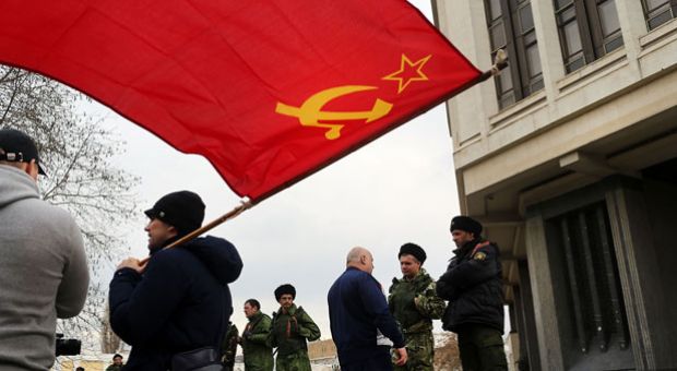 A man holds a Soviet-era flag as dozens of Russian Cossacks surround the parliament building in a show of support for Russia on March 6, 2014 in Simferopol, Ukraine. Dozens of Russian Cossacks surrounded the building in a show of support for Russia. As the standoff between the Russian military and Ukrainian forces continues in Ukraine's Crimean peninsula, world leaders are pushing for a diplomatic solution to the escalating situation. Crimean citizens will vote in a referendum on 16 March on whether to become part of the Russian federation. 