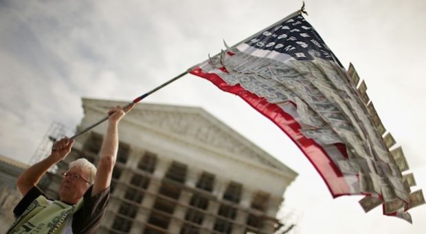David Barrows, of Washington, DC, waves a flag with corporate logos and fake money during a rally against money in politics outside the Supreme Court October 8, 2013 in Washington, DC. On Tuesday, the Supreme Court heard oral arguments in McCutcheon v. Federal Election Committee, a first amendment case that will determine how much money an individual can contribute directly to political campaigns. (Photo by Chip Somodevilla/Getty Images)