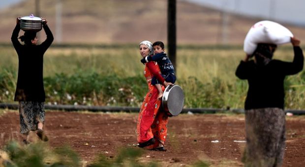 Kurdish women, one carrying a child, walk past farm land along the border area, close to the southeastern village of Mursitpinar, in the Turkish Sanliurfa province, opposite the Syrian town of Kobane, also known as Ain al-Arab, where heavy fighting between Islamic State (IS) militants and Kurdish fighters is taking place, on October 16, 2014. Turkey's ruling party said it was optimistic about the prospects for the peace process with Kurdish rebels after a spate of violence raised concern about its viability. AFP PHOTO / ARIS MESSINIS 